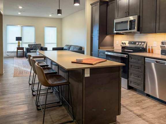 Open kitchen with island seating, dark cabinets, and stainless steel appliances.