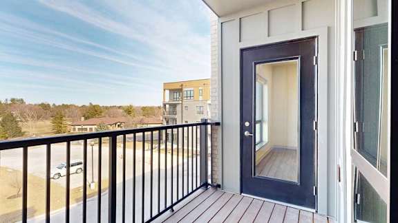 A balcony with a metal railing, a windowed door to the living room, and a view of the neighborhood.