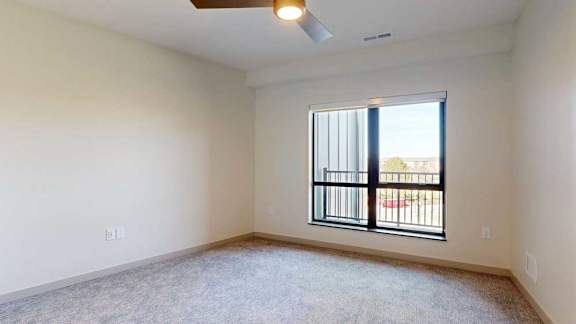 A bedroom with a large floor-to-ceiling window, a ceiling fan, and carpeted flooring.