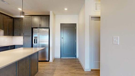A front entryway next to a modern kitchen with dark cabinets and stainless steel appliances.