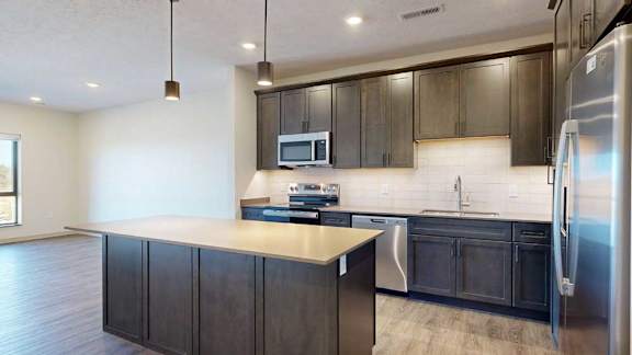 A kitchen with dark wooden cabinets, quartz countertops, an island, and stainless steel appliances.