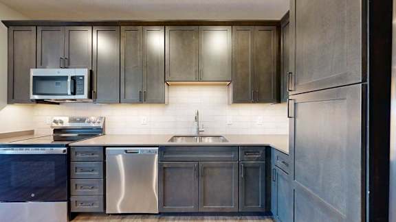 A modern kitchen sink with quartz counters, dark wooden cabinets, and a tile backsplash.