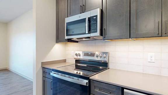 A close up of the stainless steel microwave and range in a kitchen with dark wooden cabinets.