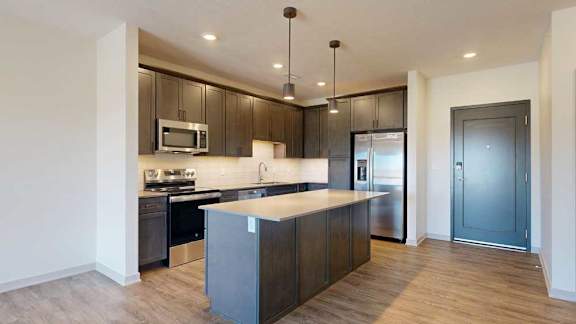 A kitchen with dark wooden cabinets, quartz countertops, an island, and stainless steel appliances.