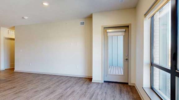A living room with hardwood-style flooring, floor-to-ceiling windows, and a windowed door to a balcony.