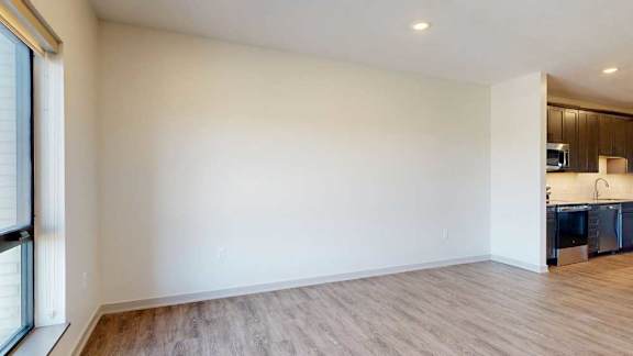 A living room with hardwood-style flooring and kitchen with dark wooden cabinets.