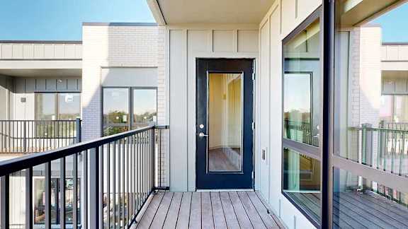 A balcony with a black metal railing and a windowed door to the living room, overlooking the courtyard.