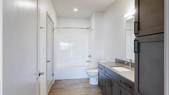 A bathroom with a wide vanity sink, dark wood cabinets, and a tub shower.