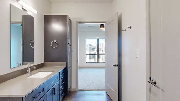 A bathroom with a wide vanity sink, mirror with overhead lighting, and a tall storage cabinet.