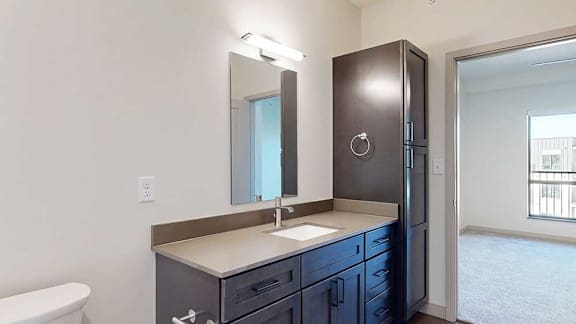 A bathroom with a wide vanity sink, mirror with overhead lighting, and a tall storage cabinet.