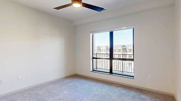 A bedroom with a ceiling fan and an oversized window overlooking a balcony.