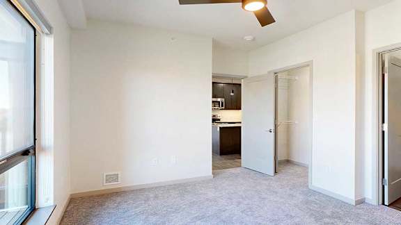 A bedroom with a ceiling fan, a large window for plenty of natural light, a walk-in closet, and an attached bathroom.