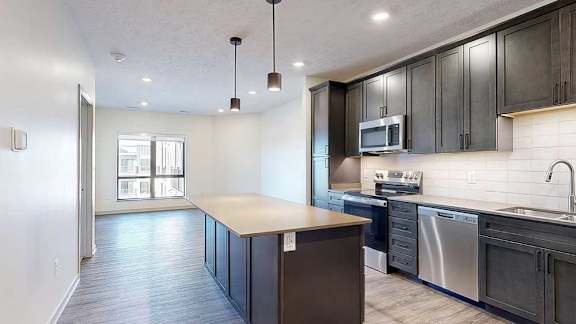 A kitchen with dark wooden cabinets and a large central island in front of an open living room.