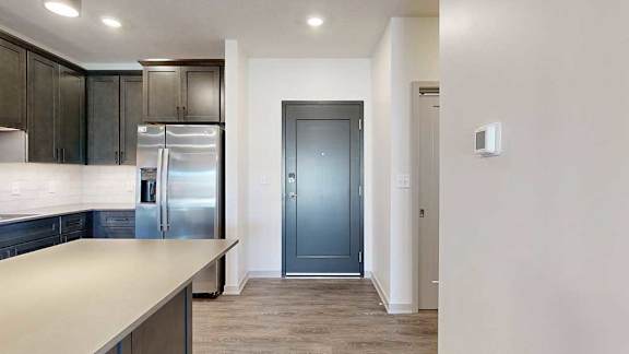 A dark grey front door next to a modern kitchen with dark wooden cabinets.