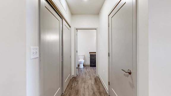 A hallway with a doors on either side, and an open door to a bathroom at the end.