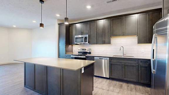 A modern kitchen with stainless steel appliances, quartz countertops, a central island, and dark wooden cabinets.