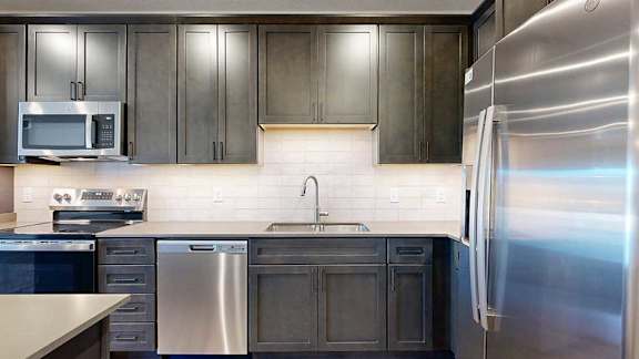 A modern kitchen with dark wood cabinets, a tile backsplash, and stainless steel appliances.
