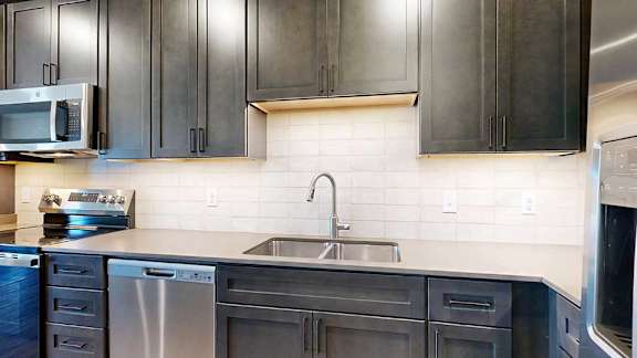 A modern kitchen with stainless steel appliances, quartz countertops, and dark wooden cabinets.