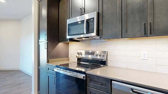 A stainless steel range and microwave in a modern kitchen with tile backsplash and dark wooden cabinets.