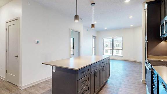 A modern kitchen with a large central island with dark wooden cabinets, and pendant lighting.