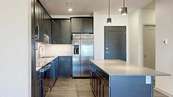 A modern kitchen with stainless steel appliances, quartz countertops, a central island, and dark wooden cabinets.