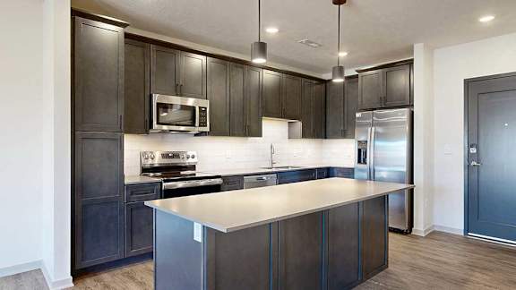 A modern kitchen with stainless steel appliances, quartz countertops, a central island, and dark wooden cabinets.