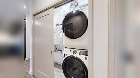 A double door closet in the hallway with a stacked full-sized washer and dryer.
