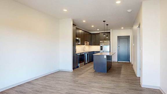 A living room with hardwood flooring open to a modern kitchen with dark cabinets.