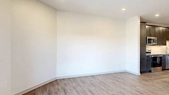 A living room with hardwood flooring open to a modern kitchen with dark cabinets.