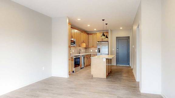 an open living room with hardwood flooring next to a kitchen with wooden cabinets and a large central island
