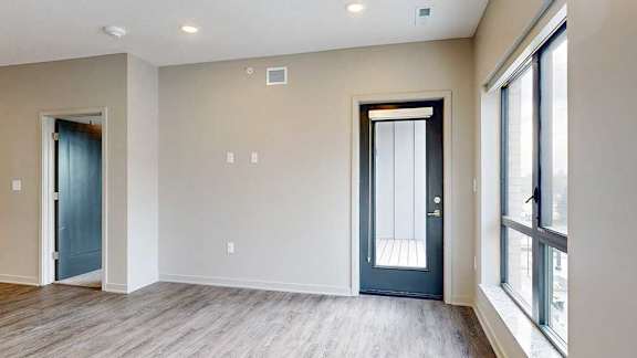 a living room with hardwood flooring, a large window, and a door to the balcony