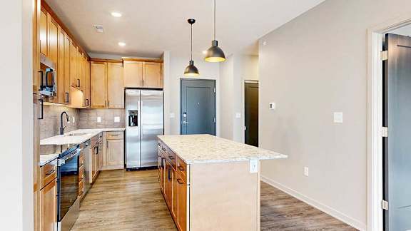 a modern kitchen with wooden cabinets, quartz countertops, a tile backsplash, under cabinet lighting, stainless steel appliances, and a large central island