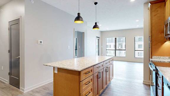 a kitchen with a large central island with cabinets, quartz countertop, and pendant lighting