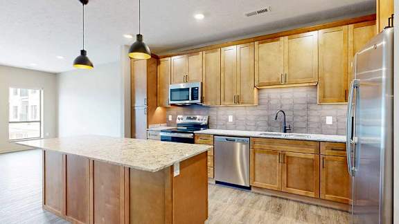 a modern kitchen with wooden cabinets, quartz countertops, a tile backsplash, under cabinet lighting, and stainless steel appliances