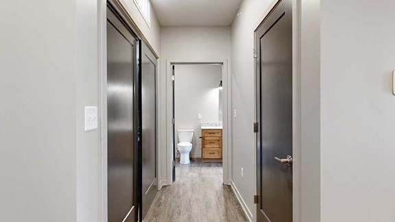 a hallway with doors on either side, leading to an open door to a bathroom