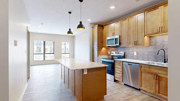 a kitchen with wooden cabinets and a large island in front of an open living room with large windows