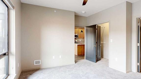a carpeted bedroom with a ceiling fan, a walk-in closet, and a large window