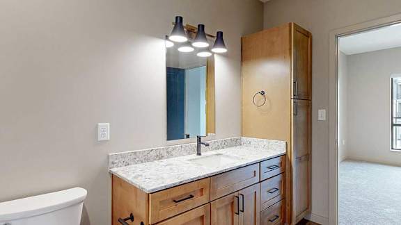 a walk-through bathroom with a quartz vanity sink, tall storage cabinet, and mirror with overhead lighting