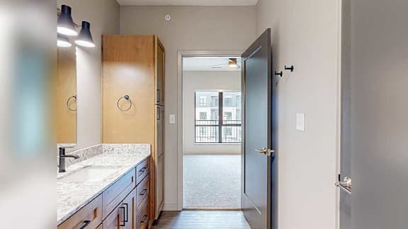 a bathroom with a quartz vanity sink, mirror, and a door leading to the bedroom