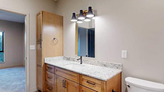 a bathroom with tan cabinets, a quartz vanity sink, and a tall storage cabinet