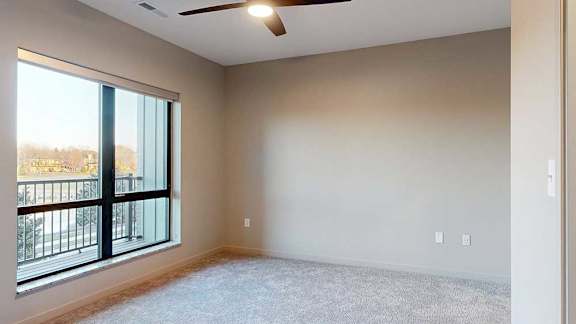 a bedroom with a ceiling fan and a large window overlooking a balcony