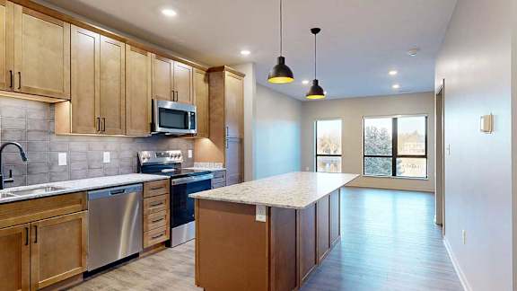 a kitchen with a large central island featuring tan wooden cabinets and light quartz countertops