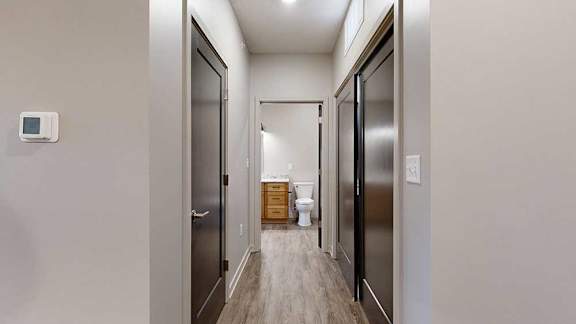 a hallway with a storage closet and the laundry closet, leading to an open door to the bathroom