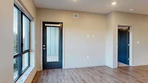 a living room with hardwood flooring, a large window, and a windowed door to the balcony