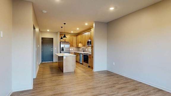 an open concept living room next to a kitchen with tan wooden cabinets, quartz countertops, and stainless steel appliances