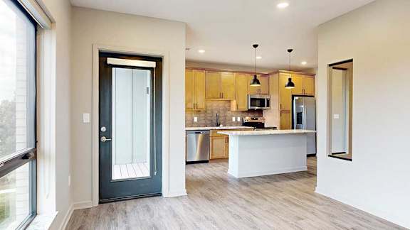 A living room with hardwood flooring and a windowed door to the balcony, adjacent to the sleeping area privacy wall and kitchen.