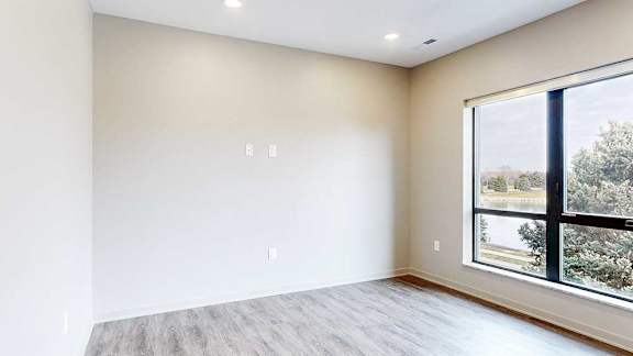 Living room with wood-style flooring and corner window, located next to the balcony door.