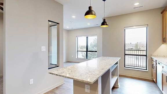 Kitchen island with quartz countertop and pendant lighting, positioned beside a large window overlooking the balcony area.