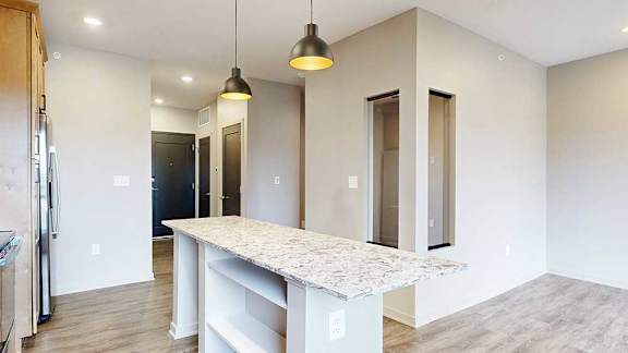 Kitchen island with open shelving on the end, pendant lights above, and carpeted sleeping area beyond.