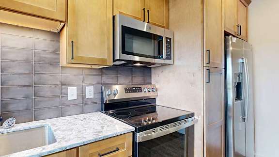Close-up of stainless steel microwave and stove set into wood cabinetry with tiled backsplash.